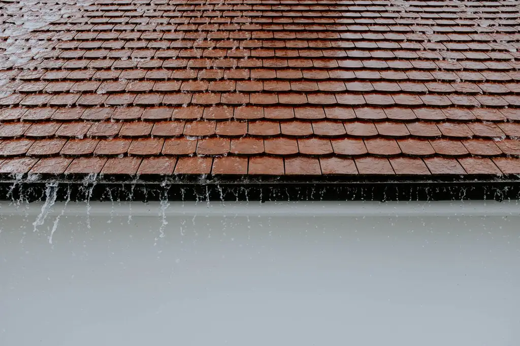 Rainwater cascading off the edge of a house roof toward the gutter below.